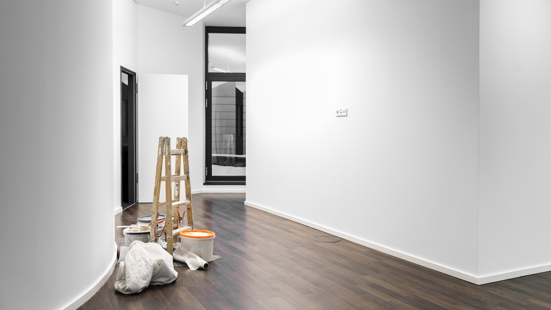 Eine leere, frisch gestrichene weiße Galerie mit Holzboden und einer Leiter.